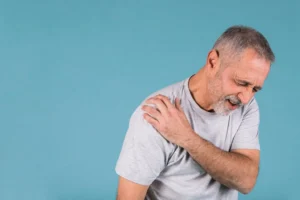 Stressed senior man with shoulder arthritis pain on blue backdrop